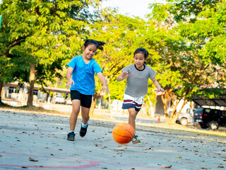 Two young girls playing basketball together on outdoor court