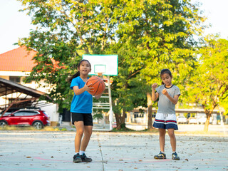 Two young girls playing basketball together on outdoor court