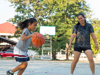 Mother and daughter played basketball together on an outdoor court during sunset.