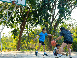 Happy Asian family playing basketball together on outdoor court at the park during golden hour.