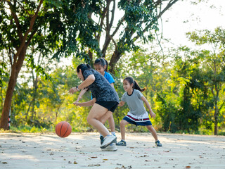 Happy Asian family playing basketball together on outdoor court at the park during golden hour.