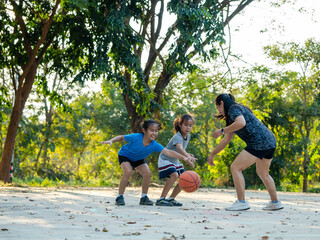 Happy Asian family playing basketball together on outdoor court at the park during golden hour.