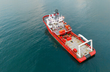 Drone shot looking down at a red offshore supply ship moving through the turquoise water featuring details of the deck and crane equipment used for marine research operations