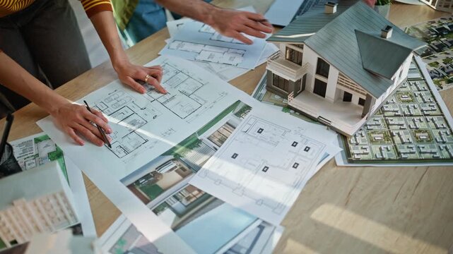 Architects hands pointing blueprints analyzing building model at office closeup.