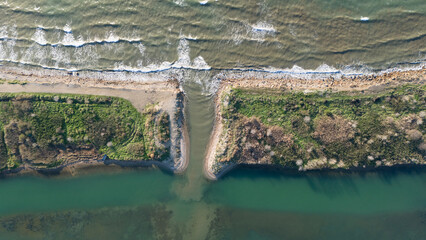 Top down aerial view of a river mouth meeting the sea where muddy brown water mixes with the green ocean water showing natural sediment patterns and coastal texture © Buğra Kaan Ersoy