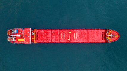 Top down panoramic view of a massive red cargo ship sailing vertically in the frame emphasizing the scale of the vessel against the deep blue ocean water texture © Buğra Kaan Ersoy