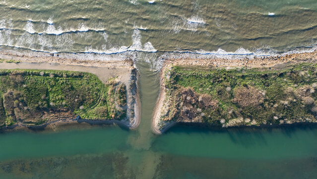Top down aerial view of a river mouth meeting the sea where muddy brown water mixes with the green ocean water showing natural sediment patterns and coastal texture