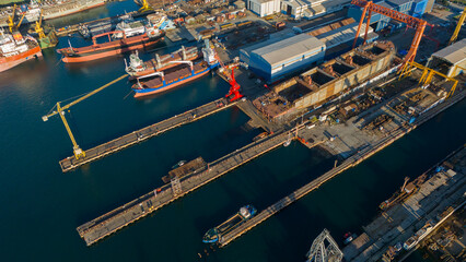 Aerial view of large yellow cranes standing on the pier of a shipyard ready to lift heavy loads for ship repair and construction projects in a sunny industrial setting