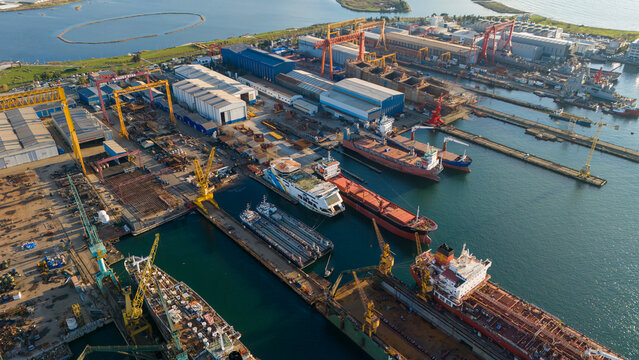 Drone view of a crowded industrial pier with multiple ships tied up including cargo vessels and tugboats emphasizing the busy nature of the maritime logistics sector