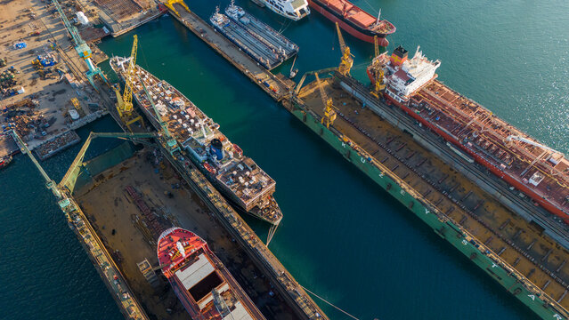 Aerial shot of a shipyard dock containing a blue and white passenger ship undergoing renovation next to a large orange tanker showing variety in marine industry