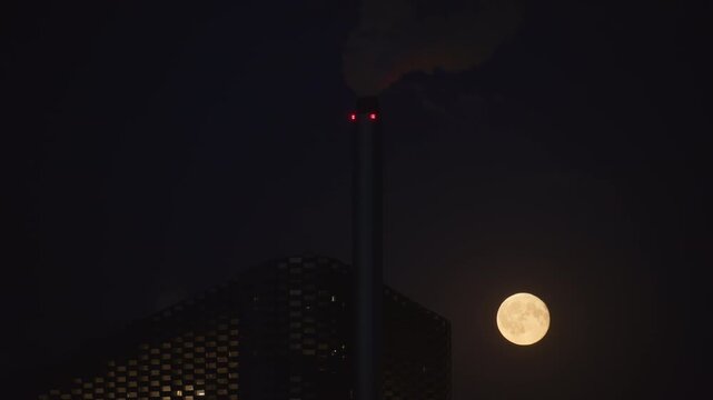 Full moon illuminating the Copenhill Amager Bakke waste to energy plant and its chimney at night. Copenhagen, Denmark