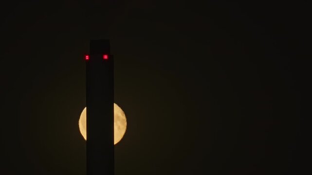 Tall Copenhill chimney building tower silhouetting a large full moon in a dramatic dark sky. Copenhagen, Denmark