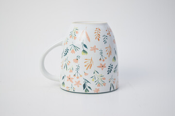 Inverted white ceramic mug with colorful autumn leaf and flower patterns on white background