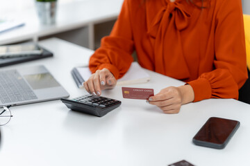 Balancing Budget: A focused individual meticulously manages finances, using a calculator and card to navigate the intricate world of numbers at desk.