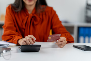 Financial Planning and Calculations: Focused view of a lady using a credit card and calculator to review and manage the budget and personal finances, against a modern backdrop.