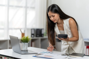Focused Calculation: A businesswoman in an organized office space meticulously reviews financial data, calculator in hand, embodying professionalism and dedication. 