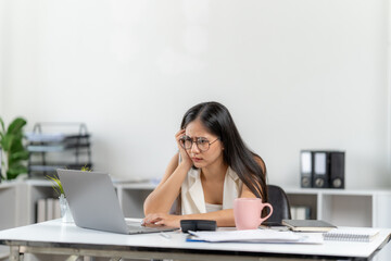 Overwhelmed: An Asian woman, at her desk, faces the stresses of modern work life, struggling with a laptop. Her weary expression hints at the pressure, deadlines, and challenges that define her work