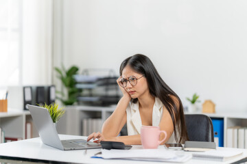 Workday weariness: a woman working on a laptop computer seems exhausted by her work and looks very tired, demonstrating a heavy workload and its mental weight on the worker.