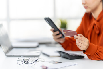 Online Payment: A person meticulously enters their credit card details on a smartphone, poised amidst a modern work environment, as the laptop sits open.
