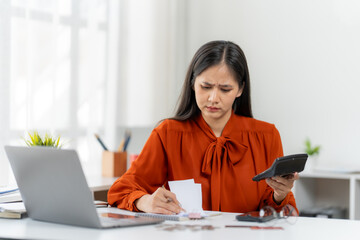 Financial Dilemma: A woman is engrossed in managing expenses, with a calculating instrument and paper materials, reflecting on a feeling of stress and uncertainty in the face of financial challenges.