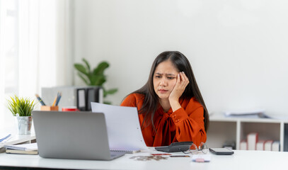 Financial Frustration: A woman, immersed in a sea of paperwork and a looming financial strain, expresses a moment of reflection and hardship amidst a backdrop of bills and calculations.
