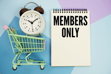 Members Only text written on notepad with alarm clock and trolley shopping cart