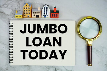 Jumbo Loan Today text written on notepad with house model and magnifying glass on marble background