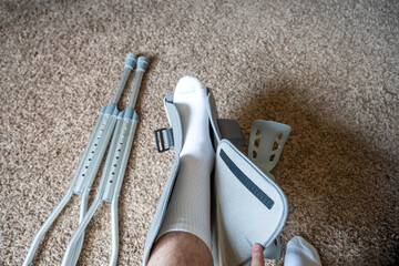 Leg brace and crutches placed on carpet with a foot resting near them during recovery time at home