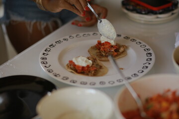 Hand spooning yogurt onto nachos, close-up food preparation scene with focus on texture and movement