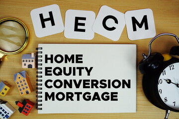 HECM Home Equity Conversion Mortgage text written on notepad with house model, alarm clock and magnifying glass on wooden background
