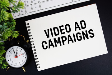 Video Ad Campaigns text written on notepad with keyboard and alarm clock on black background