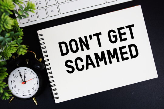 Don't Get Scammed text written on notepad with keyboard and alarm clock on black background