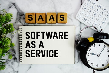 SAAS Software As A Service Is A Software text with calculator and alarm clock on marble background