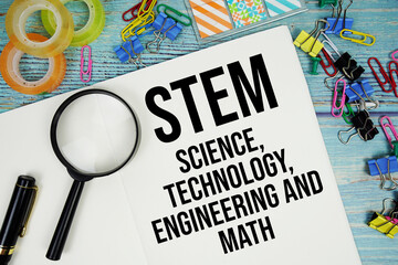 STEM Science, Technology, Engineering and Math text on a paper surrounded by office supplies and magnifying glass on a blue wooden surface