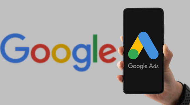 Hand holding smartphone with Google Ads on screen next to Google logo