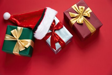 Christmas gifts and Santa hat arranged festively on a vibrant red background