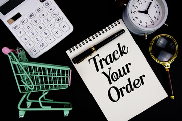 Track Your Order text written on notepad with calculator, magnifying glass, alarm clock and trolley shopping cart on black background