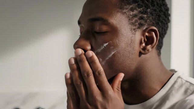  African American man applying moisturizer cream on face, men skincare and grooming concept, bathroom morning routine, healthy skin.