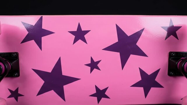 Pink Skateboard Deck Adorned with Purple Stars Illuminated by Studio Lighting on a Black Background