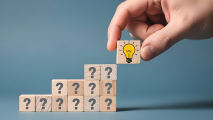 Hand placing a wooden block with a lightbulb icon on top of a pyramid of blocks with question marks
