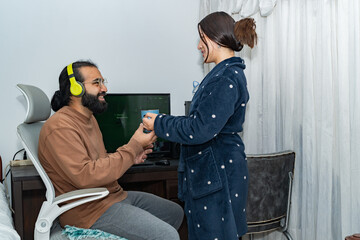 Person receiving mug at computer desk from someone in polka-dot robe