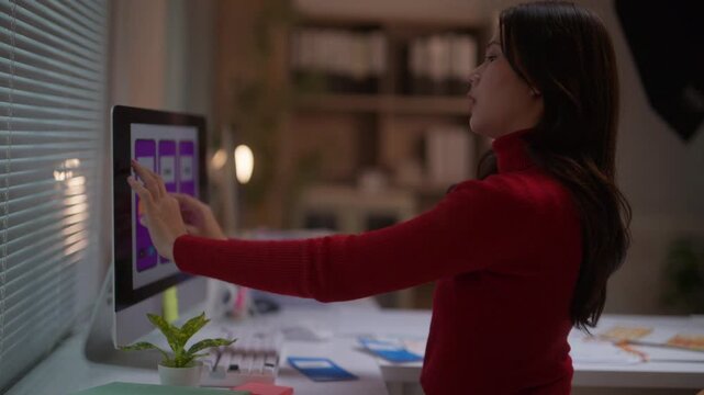 Focused Asian web developer brainstorming and creating a user experience flow for a new smartphone app. She is working late in a modern office