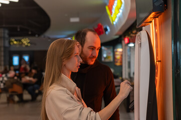 A Caucasian couple buys movie tickets at a self-service kiosk.