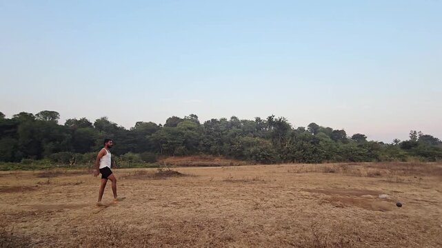 Unrecognized athlete practices shot put in a field for the Maharashtra Police exam, focusing on form. The test is crucial for recruitment into the state police force. Slow motion of body stance throw.