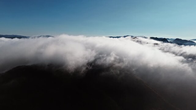 Clouds gently envelop mountain peaks under a clear blue sky in early morning