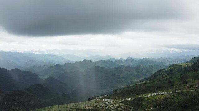 Rain shaft descending over the Mộc Ch&acirc;u tea plantations, identifying the moment localized monsoon precipitation fuels the surge of the Dải Yếm rapids and waterfalls, slow aerial shot