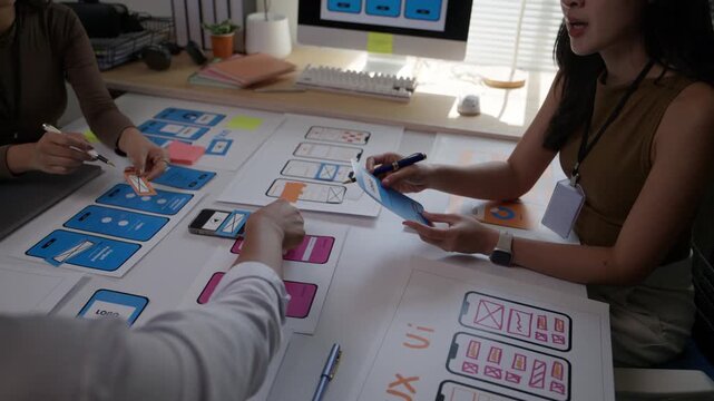 Young collaborative team of developers discussing mobile app interface design and user experience, brainstorming together in a modern office
