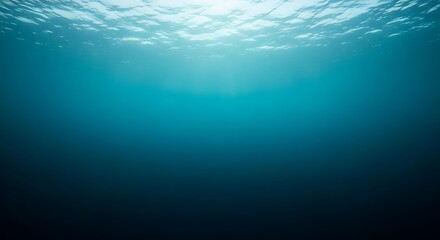 Obraz premium Underwater view looking up towards the sunlit surface, with light rays penetrating the deep blue ocean water