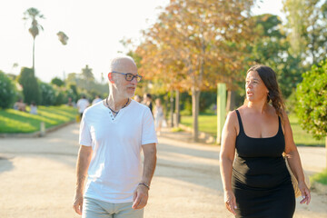 Obraz premium A man and a woman are walking together in a park. The man is wearing a white shirt and the woman is wearing a black dress. Scene is relaxed and casual