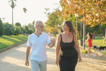 Obraz premium A man and a woman are walking together in a park. The man is wearing a white shirt and the woman is wearing a black dress. The scene is peaceful and relaxing, with people walking their dogs